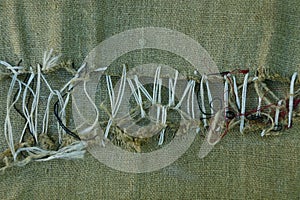 Part of a green old ragged fabric sewn with gray thread