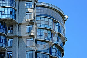 Part of a high gray house with windows and balconies against the blue sky