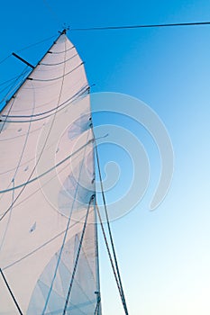 Part of hoisted mainsail of sailboat against blue sky