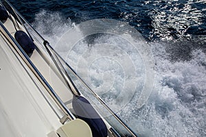 Part of the hull of the pleasure yacht with fenders against the foaming sea at full speed.