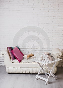 Part of interior with couch and decorative pillows, white wooden table with books on it