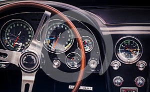 Part of the interior of an oldtimer luxury sports car with steering wheel, speedometer, fuel, clock dials, gear lever, front panel