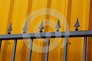 Part of the iron fence of black sharp rods against the background of the yellow wall