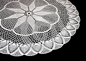 A part of isolated crocheted white doily with pattern with cones and arches a black background. Round decorative cotton doily