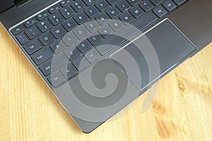 Part of laptop keyboard and touchpad of opened laptop on wooden table top view