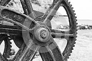 Part of a large old rusty metal wheel with jagged edges in a rotating mechanism. Black and white photo