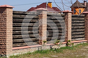 Part of a long brown fence made of bricks and wooden boards on a rural street