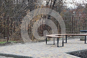 Part on a one brown wooden semicircular bench stands on a gray sidewalk