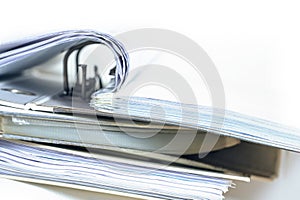 Part of an open ring binder with many documents on a stack of more file folders, business and office concept fading to a white