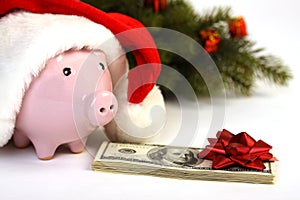 Part of piggy bank with Santa Claus hat and stack of money american hundred dollar bills with red bow and christmas tree standing