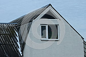 Part of a private house with an attic with a gray wall and a window under a slate roof