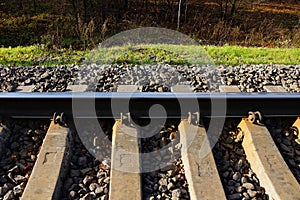 Part of the railroad with an iron rail and concrete sleepers in small gray rubble and green grass on the side of the road