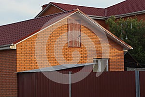 Part of a red brick house with a window and a door under a tiled roof
