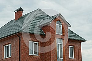 Part of a red brick house with windows under a green tiled roof
