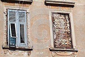 Part of residential building with old windows wooden shutters and window is walled up, closeup / Building facade elements.