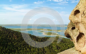 Part of the rock against the backdrop of a forested mountain slope and a panorama of a blue lake and clouds