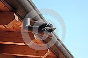 The part of roof with gutter fish shape from metal. Wooden house under the blue sky. Constructive outdoors detail.
