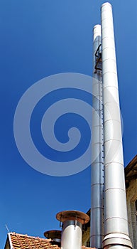 Part of the roof of an old factory building with ultra-modern stainless steel chimney against a blue sky