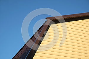 Part of rural house Wall covered with yellow siding and brown metal roof front view