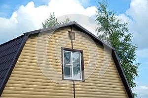 Part of rural house wall covered with yellow siding and brown metal roof front view