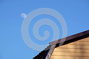 Part of rural house wall covered with yellow siding and brown metal roof and round moon in the sky front view