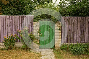 Part of a rural wooden fence and a closed green door in the grass and branches