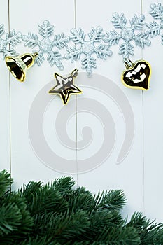 Part of spruce Christmas tree and golden ornaments and snowflakes on white wood background