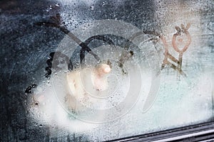 Part of steamy car window and child finger drawing from inside