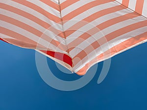 Part of a striped beach umbrella against a beautiful blue sky bottom view. Tourism and summer vacation concept