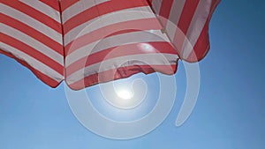 Part of a striped beach umbrella against a beautiful blue sky and sun. Tourism and summer concept