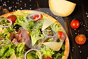 Part of Traditional Italian pizza with jamon Serrano, salad mix, cheese, black olives and cherry tomatoes.