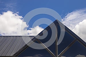 Part of the triangular roof of a modern wooden house against the bright sky in the background