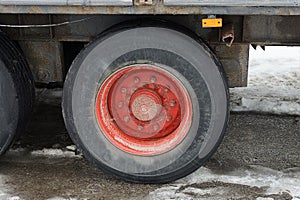 Part of a truck with one big black red wheel stands on gray asphalt