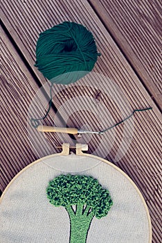 Part view of embroidery project in a hoop together with punch needle and green ball of cotton yarn on wooden ribby planks. Punch