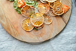 Part view of a round wooden board with dried fruits like orange, kiwi, apple, tangerine on a background of linnen fablic