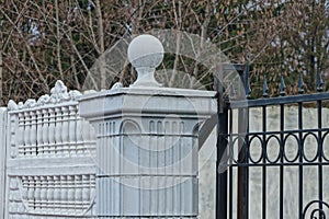 Part of a white concrete column with a stone ball in a black iron fence