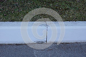 Part of a white concrete curb on a gray asphalt
