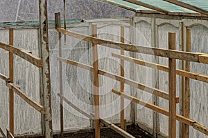 Part of a white glass greenhouse with a brown wooden grating made of boards