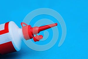 Part of a white plastic tube with a long red cap on a blue background