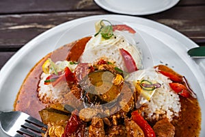 Part of white plate with sliced pork with vegetable in red sauce with rice, fork