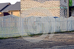 Part of a white wooden fence in the street near the road with puddles