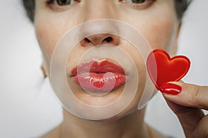 Part of a woman face. A small red heart near the woman`s lips. Kiss. Red nails