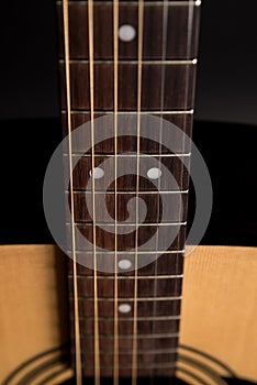 Part of a wooden acoustic guitar on a black isolated background. Vertical frame