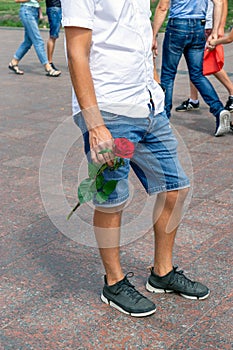 Part of a young man`s body with a flower in his hand on the street