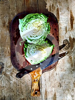 Parted cabbage with knife on a wooden plank.