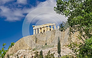 Parthenon ancient temple on acropolis hilll and green foliage trees.