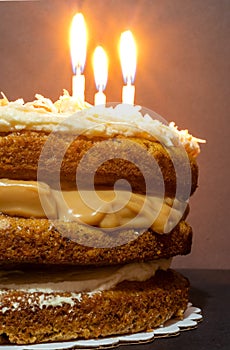 Partial close up view of carrot cake with cream chesse and coconut frosting and toffe middle with three lighted candels