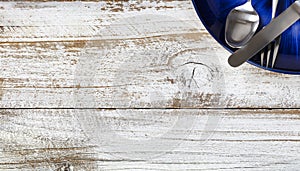 Partial dinner table setting with cutlery and dark blue plate on white rustic wood table