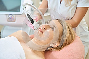 Partial female beautician doing microneedle rf lifting of skin of adult woman