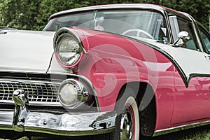 Partial front view of pink and white classic car from the fifties